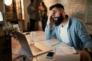 empresario-exausto-segurando-a-cabeca-com-dor-enquanto-trabalhava-ate-tarde-no-escritorio
